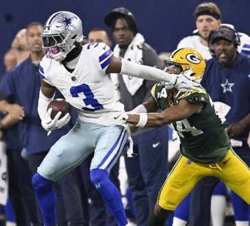 Dallas Cowboys wide receiver George Pickens holds the ball as Packers cornerback Carrington Valentine grabs him.