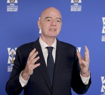 FIFA president Gianni Infantino gestures with both hands while speaking in front of a FIFA Women's World Cup backdrop.