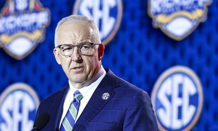 SEC Commissioner Greg Sankey speaks at a podium in front of a wall of conference logos.