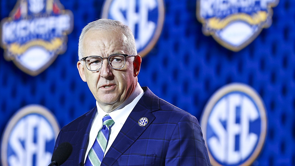 SEC Commissioner Greg Sankey speaks at a podium in front of a wall of conference logos.