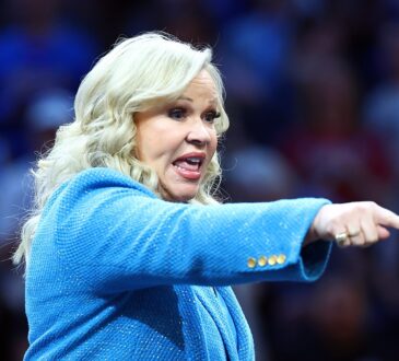 A woman in a blue blazer points toward the court during the women's national championship game.