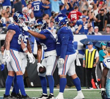 New York Giants players celebrate a touchdown in the end zone as two Dallas Cowboys defenders walk away.