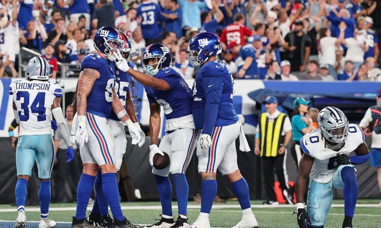 New York Giants players celebrate a touchdown in the end zone as two Dallas Cowboys defenders walk away.