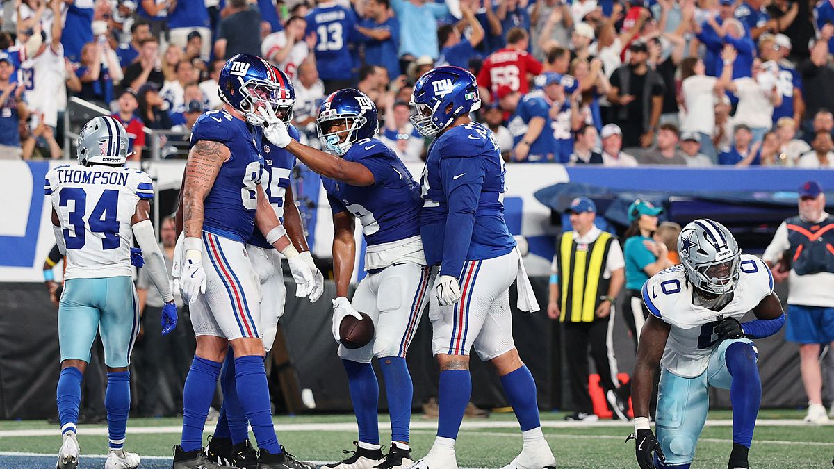 New York Giants players celebrate a touchdown in the end zone as two Dallas Cowboys defenders walk away.