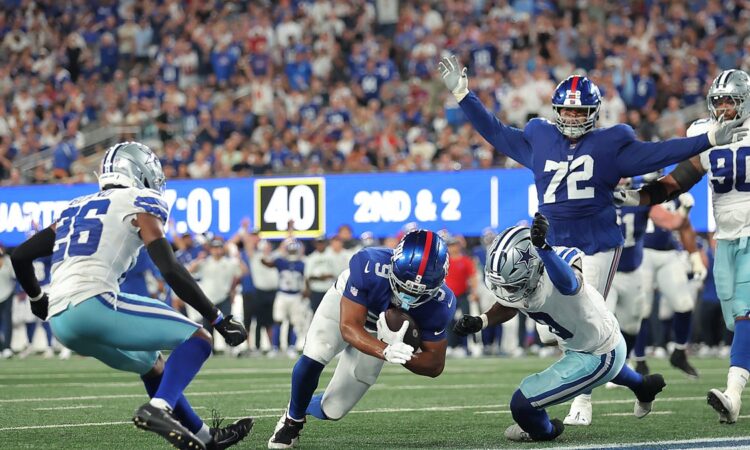 New York Giants tight end Isaiah Likely dives across the goal line as two Dallas Cowboys defenders close in.