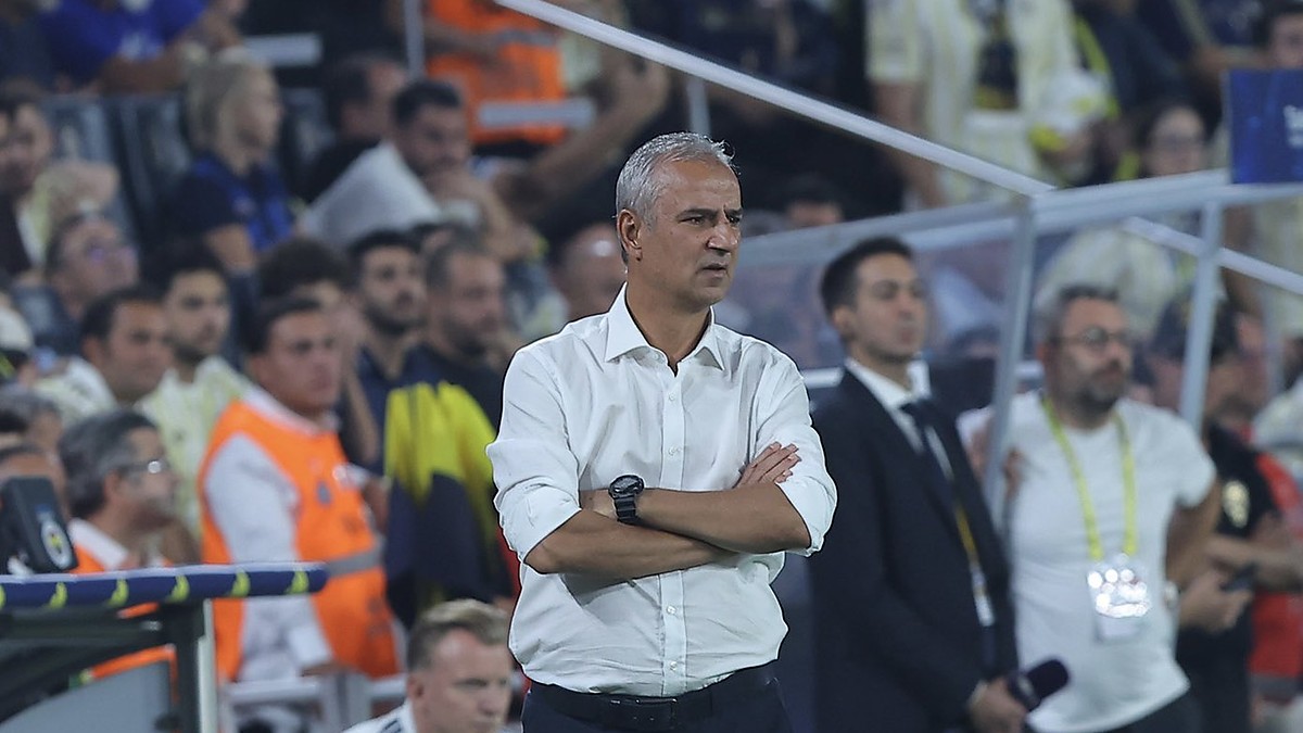 Fenerbahçe head coach İsmail Kartal stands with his arms folded on the touchline watching the match.
