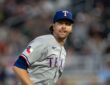 Texas Rangers starting pitcher Jacob deGrom glances to the side with his tongue at the corner of his mouth.