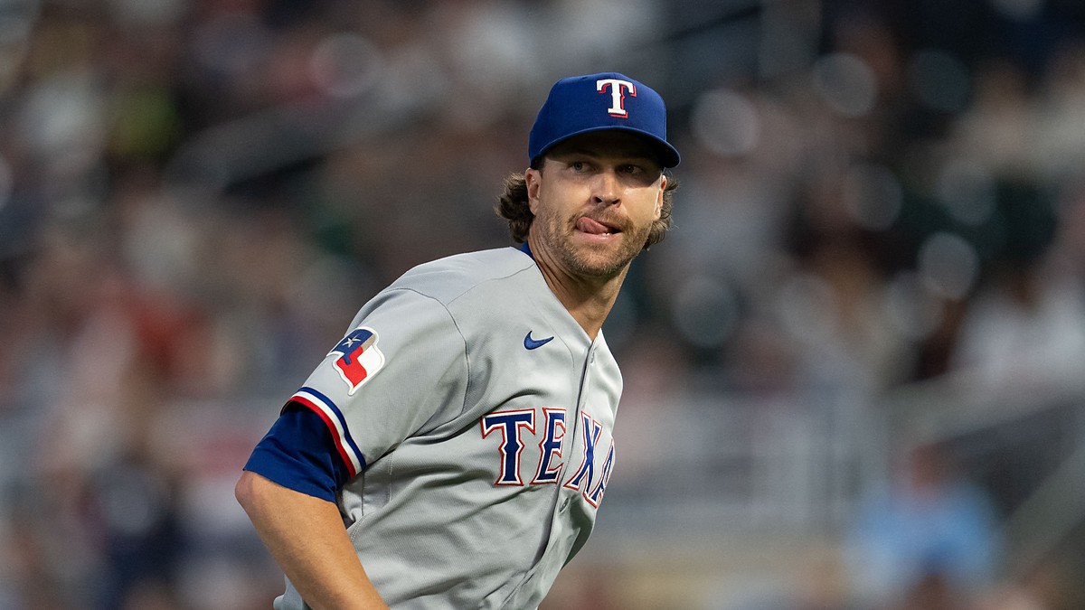 Texas Rangers starting pitcher Jacob deGrom glances to the side with his tongue at the corner of his mouth.