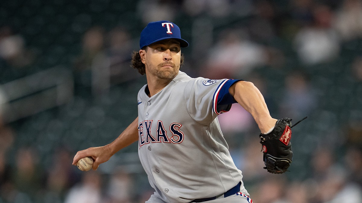 Texas Rangers starting pitcher Jacob deGrom winds up to throw a pitch in a gray road uniform and blue cap.