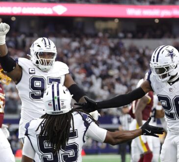 Cowboys linebacker Jaishawn Barham kneels as teammates Donovan Ezeiruaku, Kenny Clark, and DaRon Bland celebrate around him.