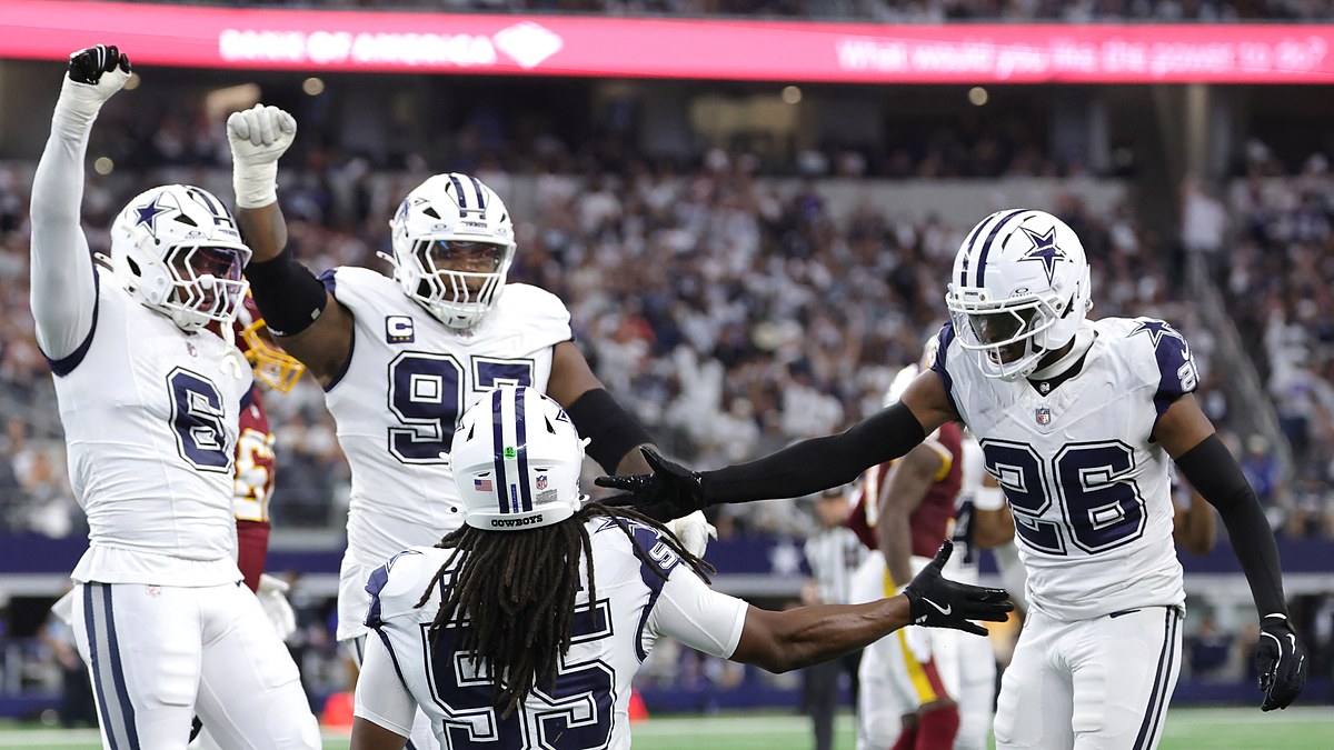 Cowboys linebacker Jaishawn Barham kneels as teammates Donovan Ezeiruaku, Kenny Clark, and DaRon Bland celebrate around him.