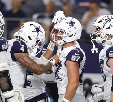Cowboys tight end Jake Ferguson smiles as teammates crowd around him to celebrate a touchdown.
