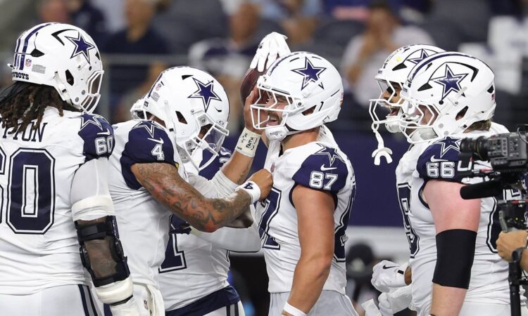 Cowboys tight end Jake Ferguson smiles as teammates crowd around him to celebrate a touchdown.