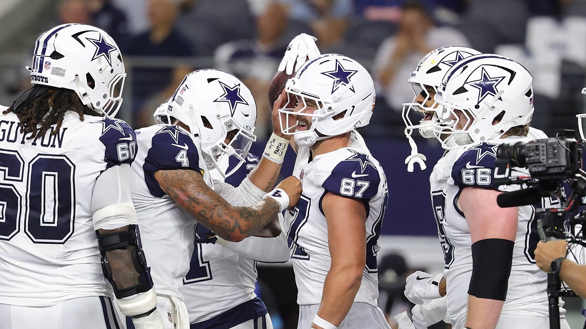Cowboys tight end Jake Ferguson smiles as teammates crowd around him to celebrate a touchdown.