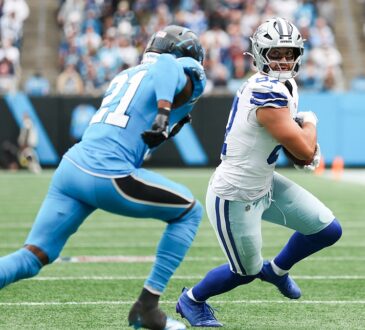 Dallas Cowboys tight end Jake Ferguson tucks the ball and looks back as a Carolina Panthers defender closes in.