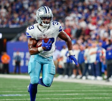 Cowboys running back Javonte Williams tucks the ball under his left arm and runs upfield along the sideline.