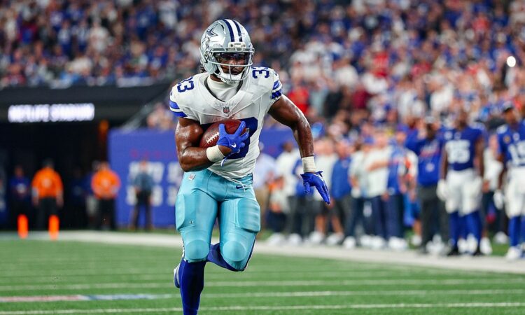 Cowboys running back Javonte Williams tucks the ball under his left arm and runs upfield along the sideline.