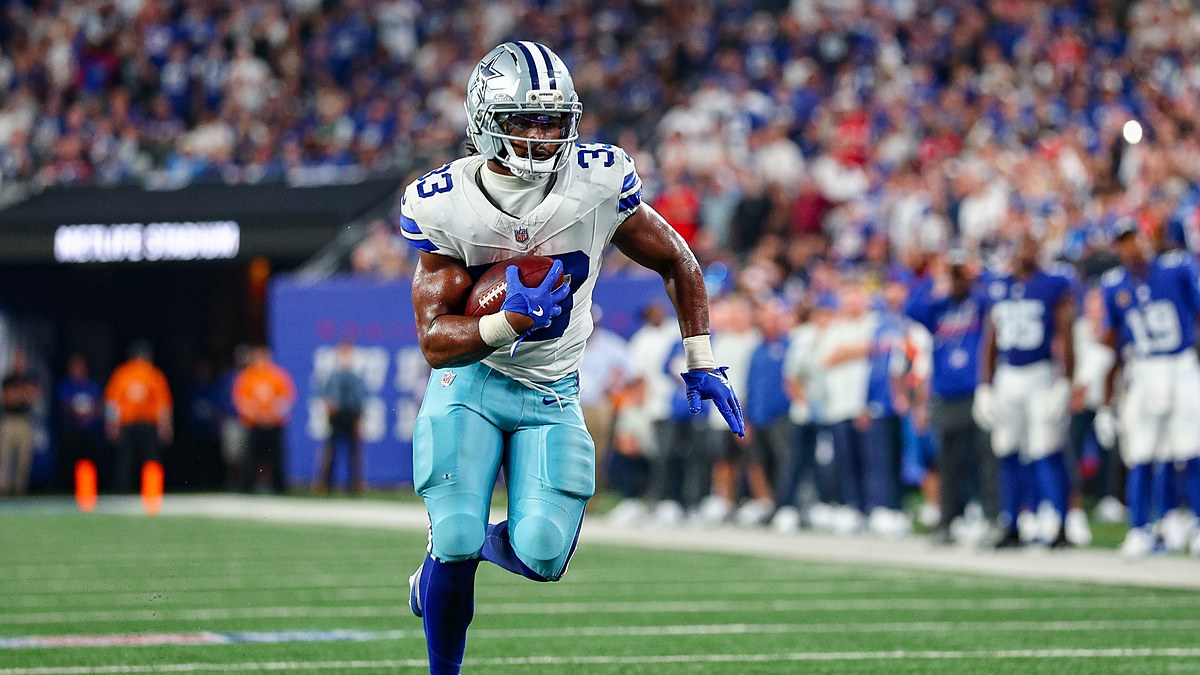 Cowboys running back Javonte Williams tucks the ball under his left arm and runs upfield along the sideline.