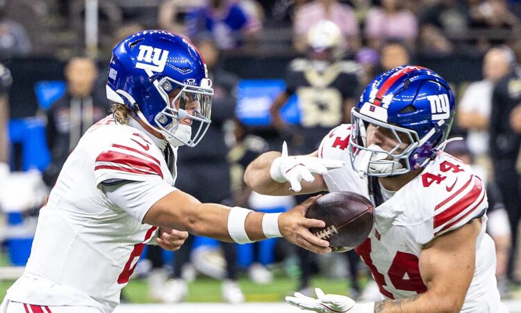 New York Giants quarterback Jaxson Dart extends the ball into running back Cam Skattebo's arms at the handoff.