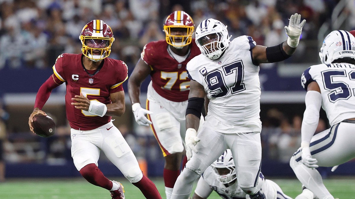 Washington Commanders quarterback Jayden Daniels scrambles with the ball as Cowboys defensive tackle Kenneth Clark closes in.