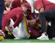 Washington Commanders quarterback Jayden Daniels lies on the field as team medical staff attend to him.