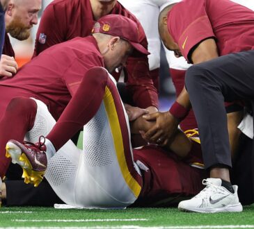Washington Commanders quarterback Jayden Daniels lies on the field as team medical staff attend to him.
