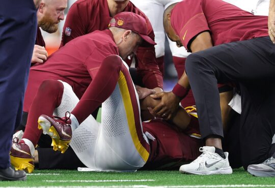 Washington Commanders quarterback Jayden Daniels lies on the field as team medical staff attend to him.
