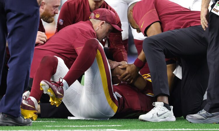 Washington Commanders quarterback Jayden Daniels lies on the field as team medical staff attend to him.