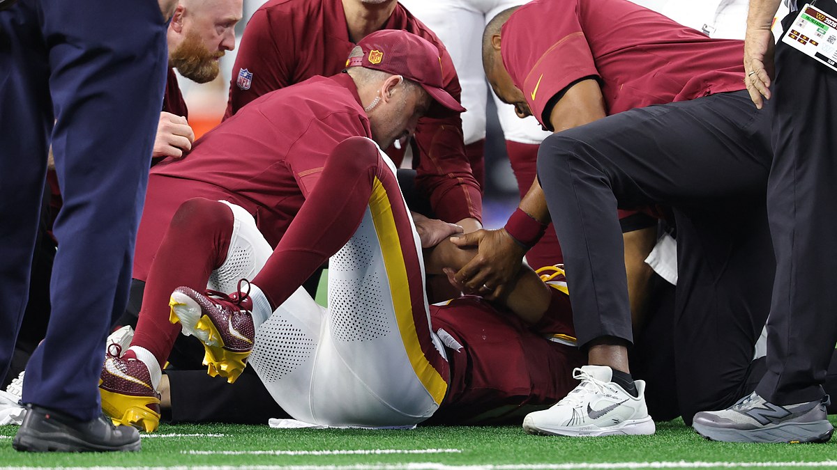 Washington Commanders quarterback Jayden Daniels lies on the field as team medical staff attend to him.