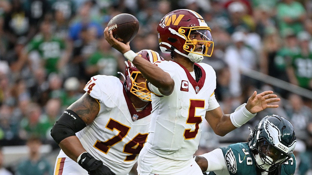 Commanders quarterback Jayden Daniels sets and releases a pass as an Eagles defender closes in from his right.