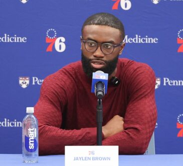 Philadelphia 76ers guard Jaylen Brown speaks at a table with a 76ers microphone and a nameplate reading Jaylen Brown.