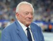 Cowboys owner Jerry Jones stands on the field in a blue suit and striped tie before kickoff.