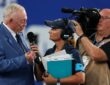 Cowboys owner Jerry Jones speaks into a handheld microphone during a sideline interview before kickoff.