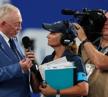 Cowboys owner Jerry Jones speaks into a handheld microphone during a sideline interview before kickoff.