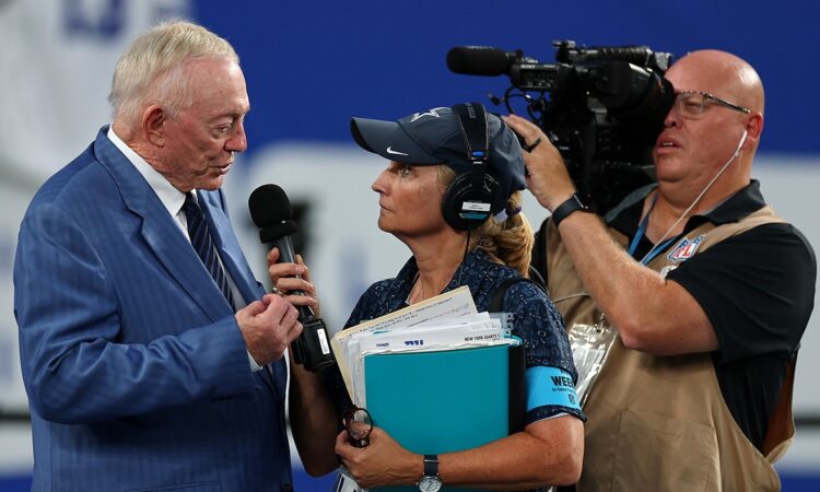 Cowboys owner Jerry Jones speaks into a handheld microphone during a sideline interview before kickoff.