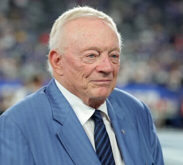 Cowboys owner Jerry Jones stands on the field in a blue suit and striped tie before kickoff.