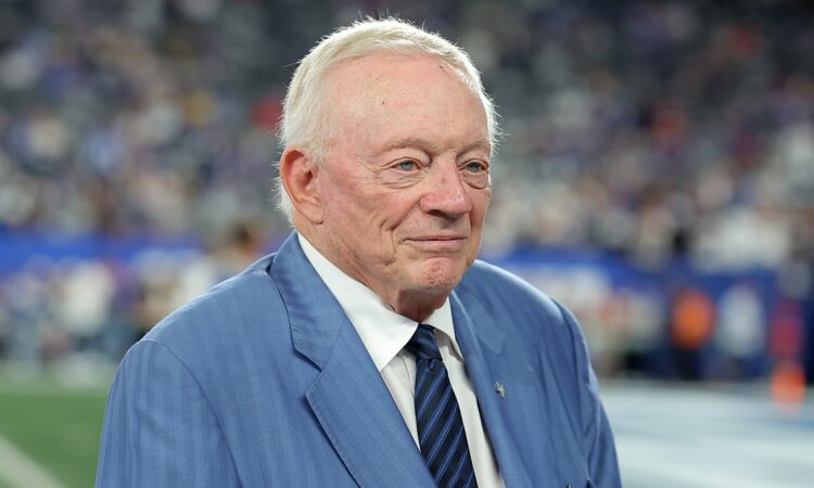 Cowboys owner Jerry Jones stands on the field in a blue suit and striped tie before kickoff.