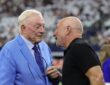 Cowboys owner Jerry Jones, in a light blue suit, talks with Jeff Bezos on the field before kickoff.