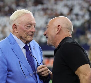 Cowboys owner Jerry Jones, in a light blue suit, talks with Jeff Bezos on the field before kickoff.