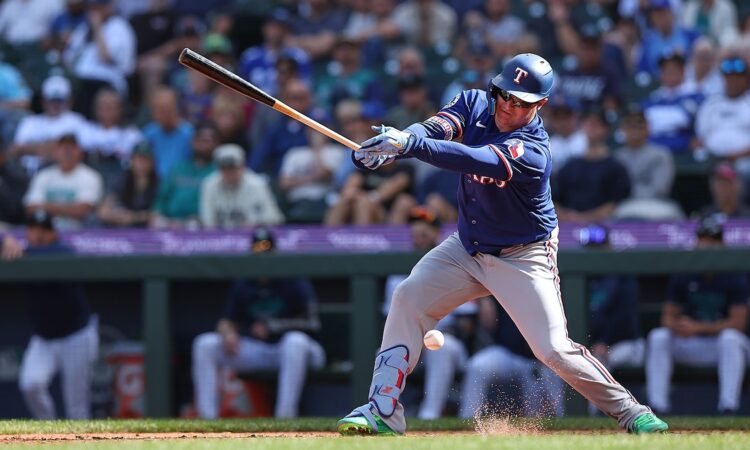 Texas Rangers designated hitter Joc Pederson swings as the ball bounces near his shin guard and dirt sprays at his feet.