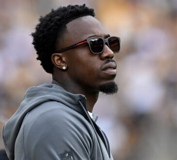 Steelers cornerback Joey Porter Jr. watches from the sideline in a hooded sweatshirt and sunglasses.