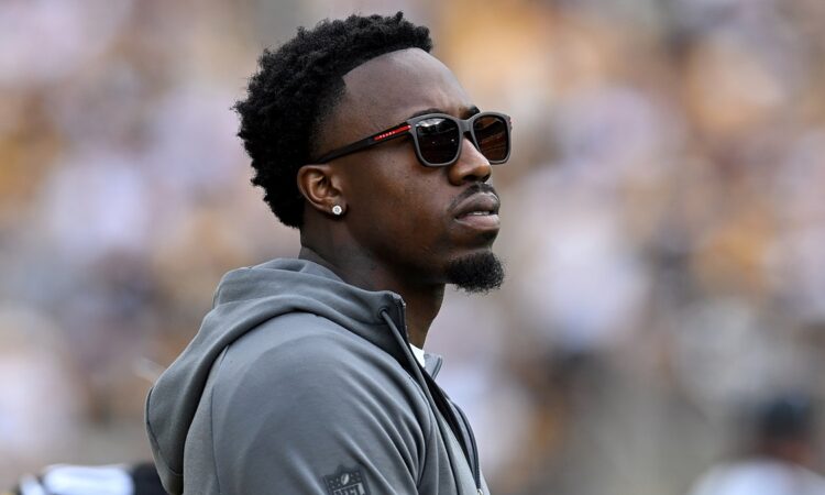 Steelers cornerback Joey Porter Jr. watches from the sideline in a hooded sweatshirt and sunglasses.