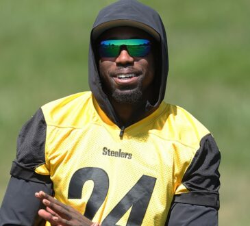 Steelers cornerback Joey Porter Jr. smiles in a hooded practice jersey while watching camp drills.