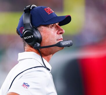 New York Giants head coach John Harbaugh looks up from the sideline wearing a headset during a game against the Jets.