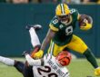 Green Bay Packers running back Josh Jacobs stiff-arms a Bengals cornerback to the ground while carrying the ball.