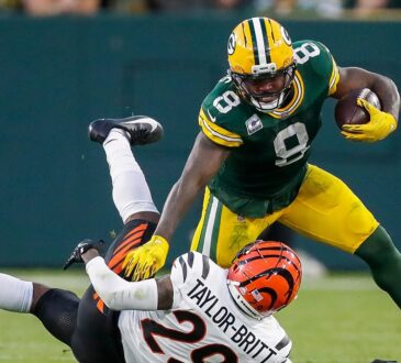 Green Bay Packers running back Josh Jacobs stiff-arms a Bengals cornerback to the ground while carrying the ball.