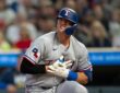 Texas Rangers designated hitter Josh Jung kneels near home plate, grimacing and clutching his gloved hand to his chest.