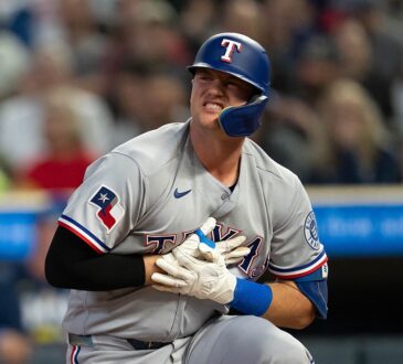 Texas Rangers designated hitter Josh Jung kneels near home plate, grimacing and clutching his gloved hand to his chest.