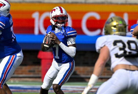 SMU quarterback Kevin Jennings drops back to pass with the ball at his chest as a UC Davis defender closes in.