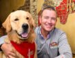 Kirk Herbstreit sits in a booth with his golden retriever Peter, who wears a red Raising Cane's bandana.